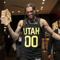 a man with dreadlocks and tattoos holding up a basketball jersey that says utah 00