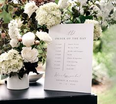 an order of the day sign next to some white flowers and greenery on a table