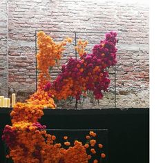 an arrangement of flowers on display in front of a brick wall with candles and vases