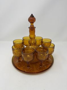 a set of yellow glass cups and a bottle on a tray with a candle holder