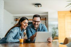 two people sitting at a table looking at something on a tablet computer while smiling and drinking orange juice