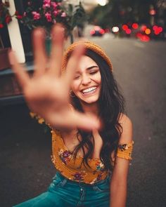 a woman sitting on the ground with her hand up in front of her face and smiling