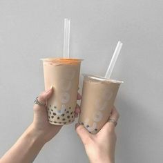 two people holding up cups with straws in each one and the other hand over them