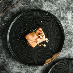 a black plate topped with a piece of food on top of a gray tablecloth