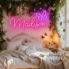 a bed with white sheets and pillows under a neon sign that says madison on it