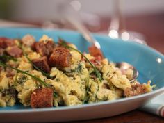 a blue bowl filled with food on top of a wooden table next to a fork