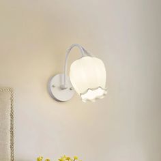 a white wall light mounted on the side of a wall next to a table with flowers