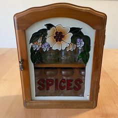 an old fashioned spice rack with jars and flowers on it, sitting on a wooden table