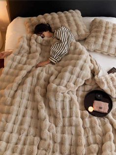 a woman laying in bed under a fluffy blanket