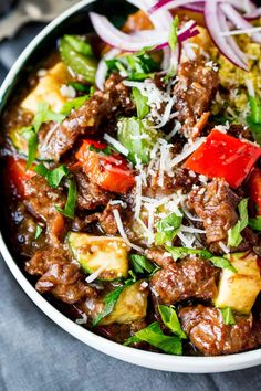 a bowl filled with meat, vegetables and grated parmesan cheese on top