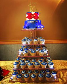 a tiered cake with cupcakes on it is decorated in blue and red