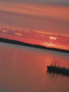 a boat floating on top of a large body of water under a cloudy sky at sunset