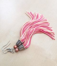 a pair of pink and silver earrings on a white surface with some beads hanging from it