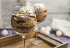 two glasses filled with dessert sitting on top of a wooden tray