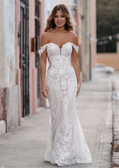 a woman in a white wedding dress is walking down the street with her hand on her hip