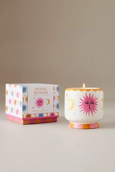 an orange blossom tea cup next to a boxed candle in a box on a table