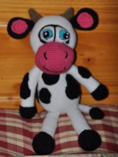 a stuffed cow sitting on top of a bed next to a wooden wall and checkered bedspread