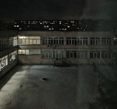 an empty parking lot at night with lights shining on the windows and buildings in the background