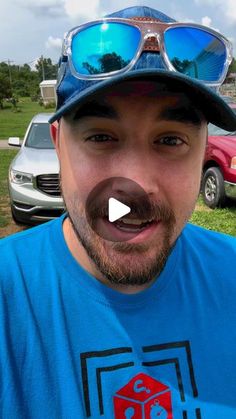 a man wearing sunglasses and a hat in front of some parked cars with his tongue out