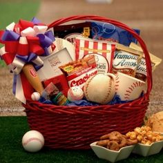 a red basket filled with baseballs, crackers and other items on top of a field