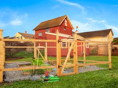 a chicken coop in front of a red house with a green lawn and fence around it