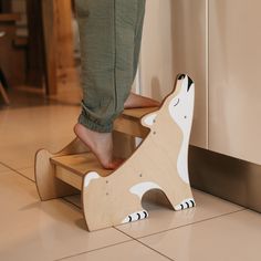 a person standing on top of a wooden toy dog next to a door and tile floor