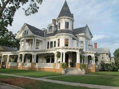 a large white victorian style house sitting on top of a lush green field