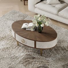 a coffee table with flowers on it in front of a white couch and rugs