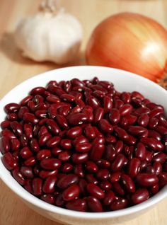 a white bowl filled with red beans next to an onion