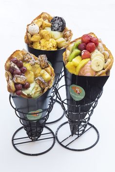 three cones filled with different types of fruit on top of metal stand holders in front of white background