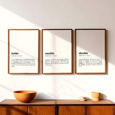 two framed posters on the wall above a wooden cabinet with a bowl and coffee cup