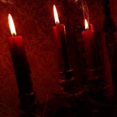 three lit candles in a dark room with red lighting on the walls and wallpaper