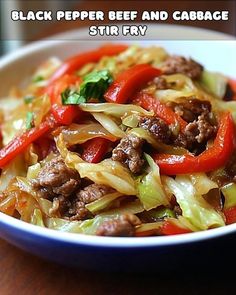 a white bowl filled with beef and cabbage stir fry on top of a wooden table