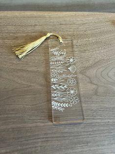 a clear bookmark with white flowers and leaves on it sitting on a wooden table