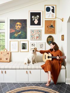 a woman sitting on top of a bench next to a white dog and holding a guitar