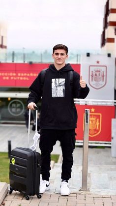 a young man is standing with his luggage and giving the thumbs up while wearing a black hoodie