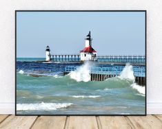 a framed photograph of a lighthouse on the ocean with waves crashing in front of it