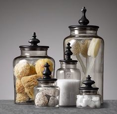 three glass jars filled with different types of bath items on top of a gray surface