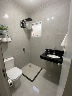 a white toilet sitting next to a sink in a bathroom under a window with a potted plant on top of it