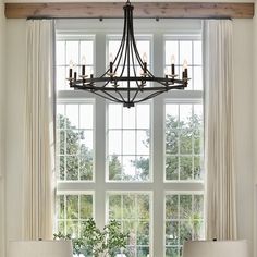 a chandelier hanging over a dining table in front of a window with curtains