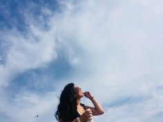 a woman standing on top of a beach next to the ocean drinking from a bottle