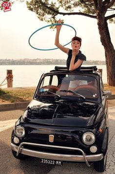 a woman holding a frisbee while sitting on top of a car