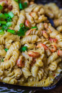 pasta with shrimp and scallions in a black bowl on a patterned table cloth