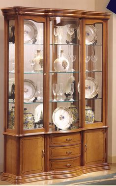 a wooden china cabinet with glass doors and plates on it's sides, in a living room