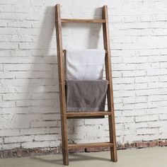 an old wooden ladder leaning against a white brick wall with a towel on it's back