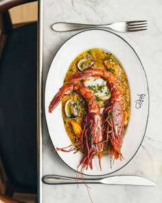 a white plate topped with seafood next to a fork and knife on top of a table