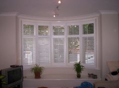 a living room with white shuttered windows and a tv in the corner next to it