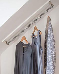 three dresses hanging on clothes racks in a room with white walls and an open window