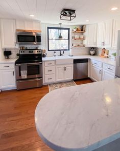 a large kitchen with white cabinets and stainless steel appliances, including an island in the middle