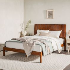 a bed with white sheets and pillows in a room next to a rug on the floor